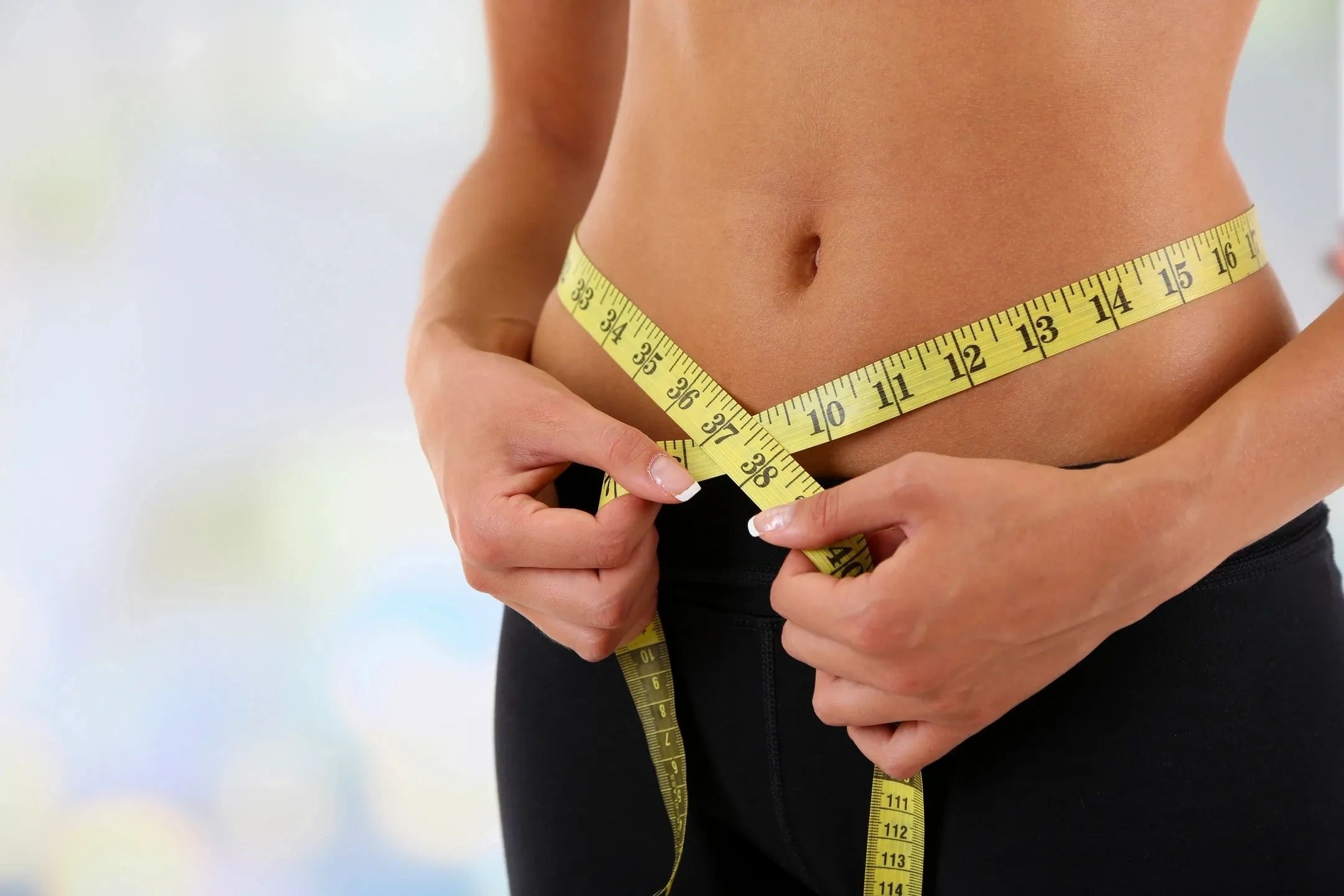Person measuring waist showing weight loss progress